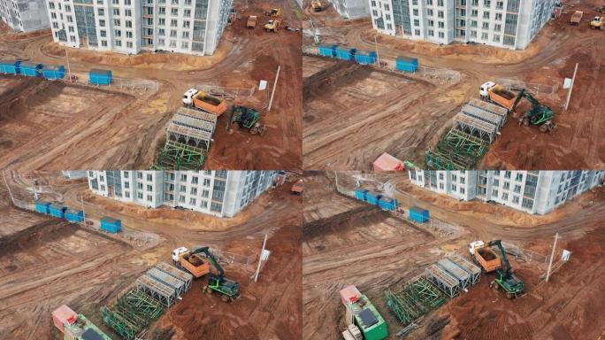 无人机挖掘机挖掘的俯视图，地面转向臂装载卡车上的沙子水泥，在大城市在建公寓楼附近的建筑工地工作的拖拉