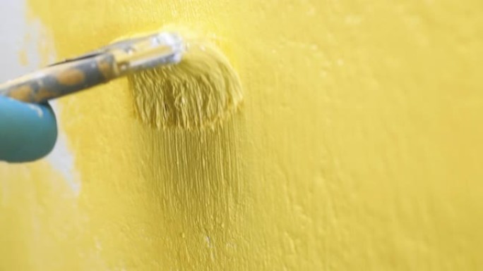 刷子在白色墙壁上上下移动，并将其涂成黄色。壁画概念。慢动作和特写视图
