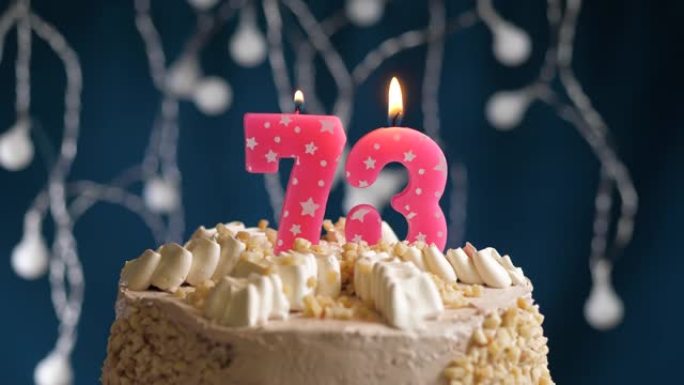 蓝色背景上有73号粉色蜡烛的生日蛋糕。蜡烛着火了。慢动作和特写视图