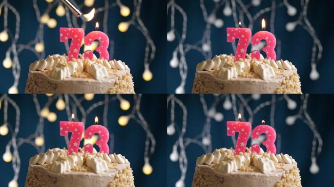 蓝色背景上有73号粉色蜡烛的生日蛋糕。蜡烛着火了。慢动作和特写视图