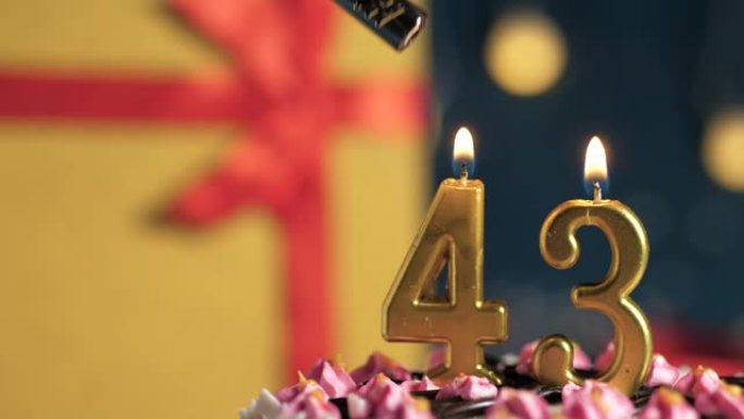 生日蛋糕编号43点灯燃烧的金色蜡烛，蓝色背景礼物黄色盒子用红丝带绑起来。特写和慢动作