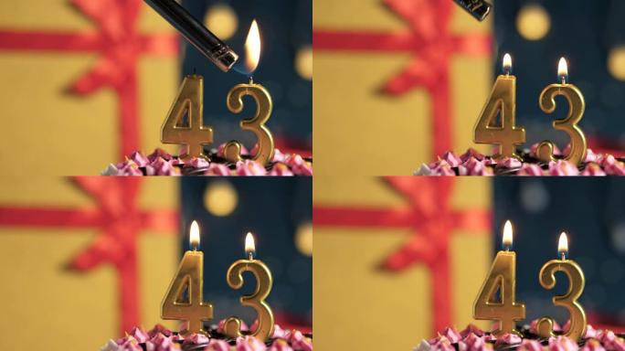 生日蛋糕编号43点灯燃烧的金色蜡烛，蓝色背景礼物黄色盒子用红丝带绑起来。特写和慢动作
