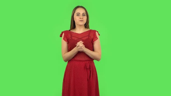 穿着红色连衣裙的温柔女孩站在令人担忧的期望中，然后松了一口气地微笑着。绿屏