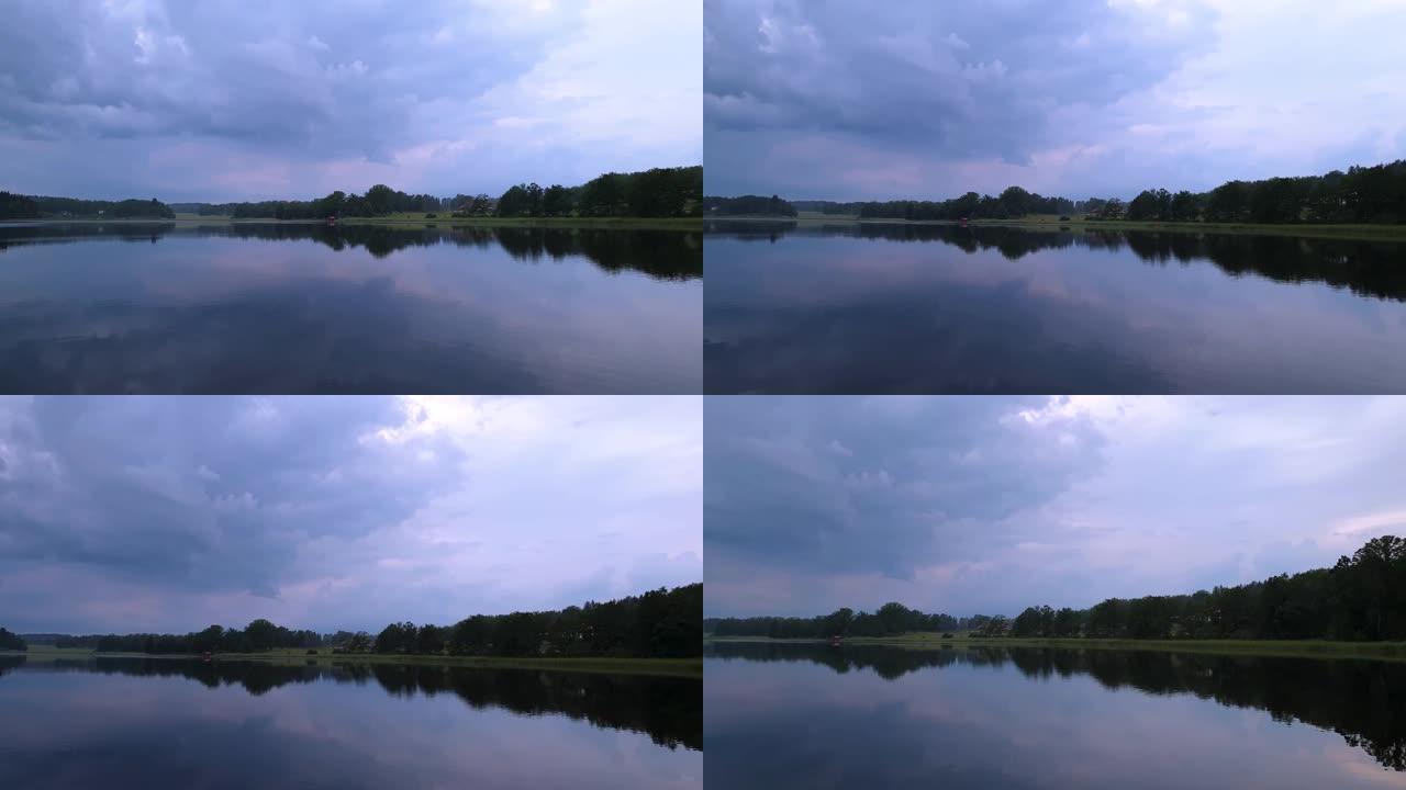 平静的夏夜日落美景。湖岸绿树和植物反射在水晶干净的镜面水面。天空覆盖着厚重的雷云。