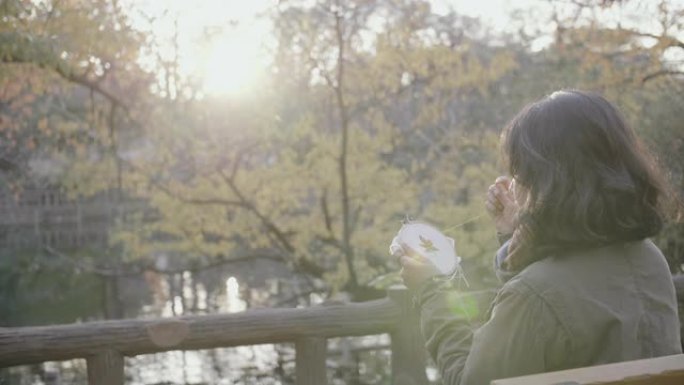 一名亚洲妇女坐在公园里，享受着枫叶图案的十字绣。