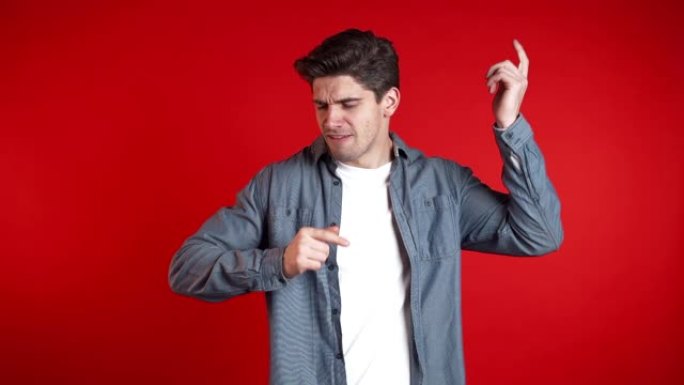 时髦的人在红色工作室背景下转向音乐。跳舞积极的喜剧演员。他用手指拨动歌曲的节奏。慢动作。