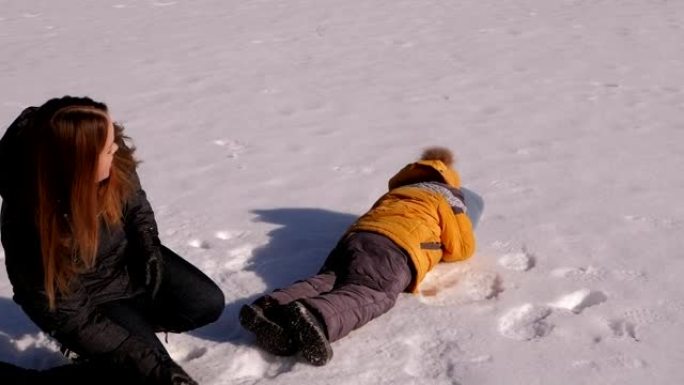 母亲带着一个小孩在打雪球，他们躺在雪地上扔雪