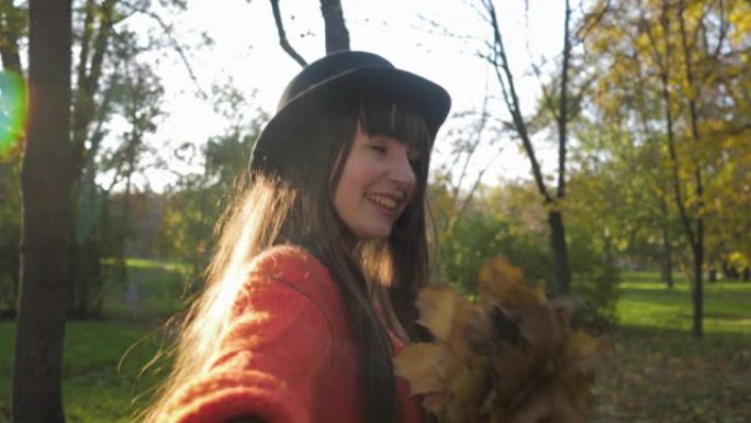 戴着长发的微笑女孩的肖像，她握着朋友的手，在落叶季节散步时带领他穿过秋天的公园