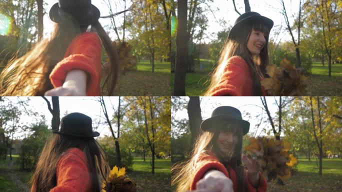 戴着长发的微笑女孩的肖像，她握着朋友的手，在落叶季节散步时带领他穿过秋天的公园