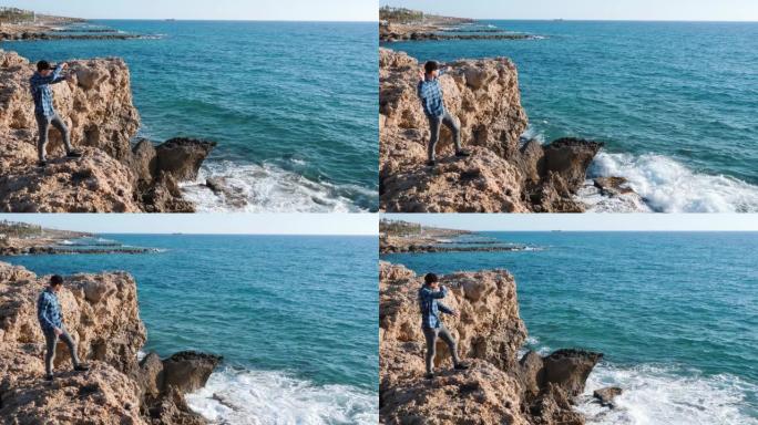 家伙把石头扔进水里。年轻人站在悬崖边，向海上扔石头。穿着蓝色衬衫和帽子的男孩站在岩石上，向悬崖边缘扔
