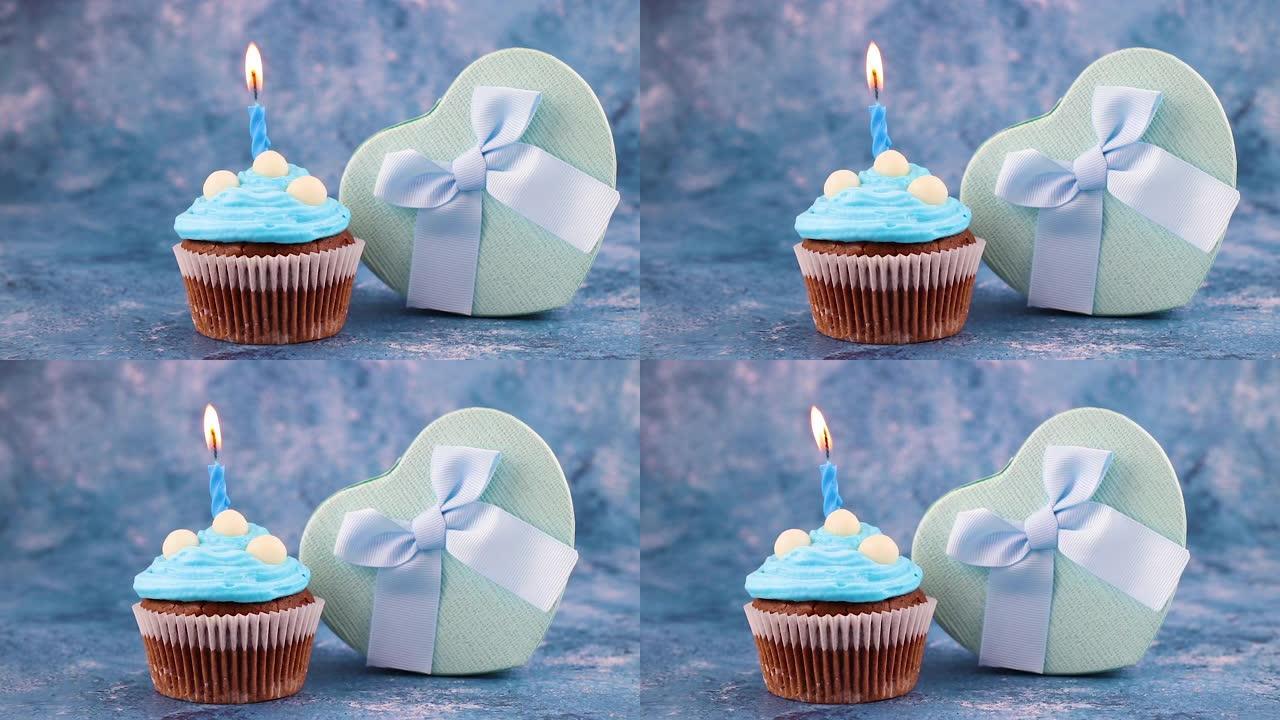 美味的生日派对美味的巧克力杯蛋糕配蓝色奶油、蜡烛和蓝色礼物