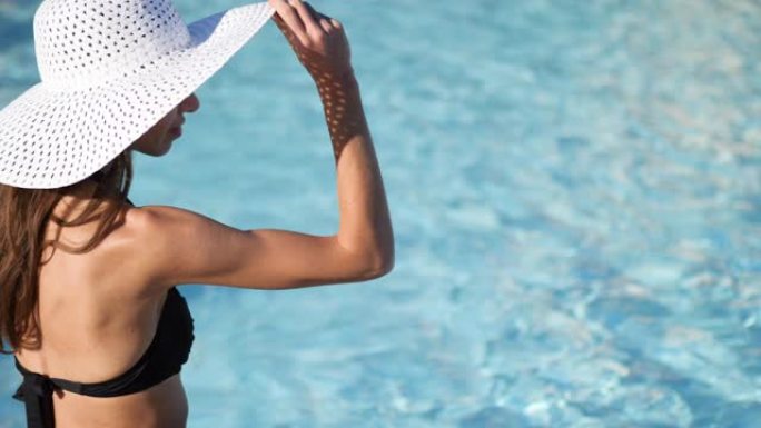 特写。模糊的水背景。一个戴着大白帽子的年轻女子坐在游泳池附近，戴着帽子。有文字的地方。ProRes 