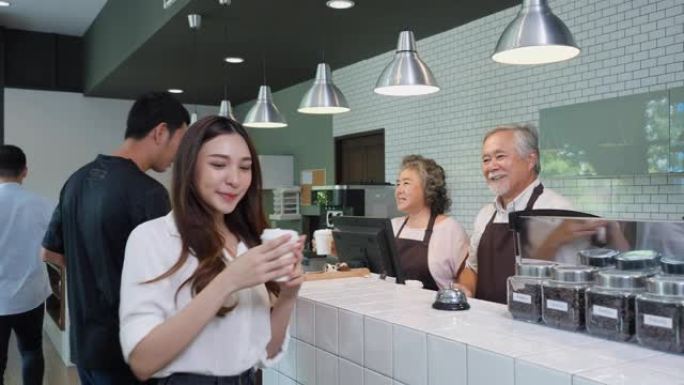 亚洲高级企业家男人和女人早上在他的咖啡店卖咖啡。亚洲人使用智能手机购买咖啡。商业、展览和表达的概念。