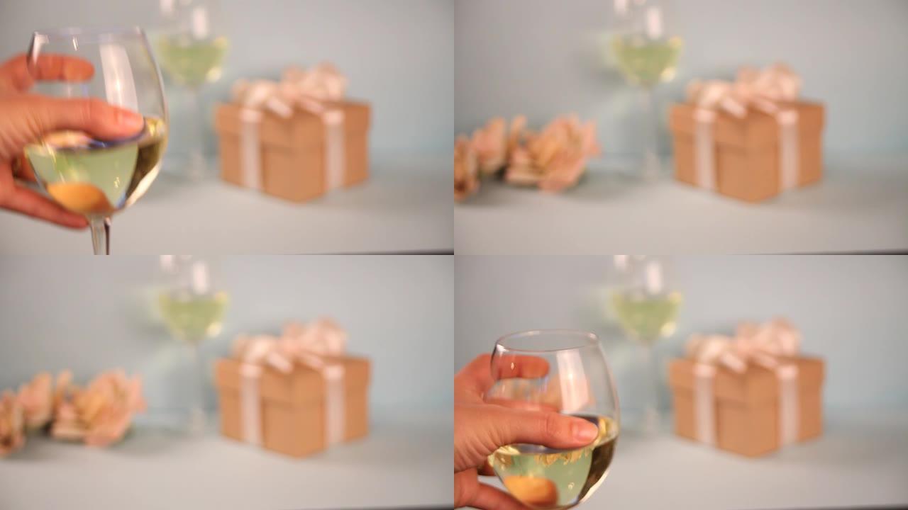 女人手放一杯白葡萄酒。背景上的礼品盒。浪漫晚餐概念