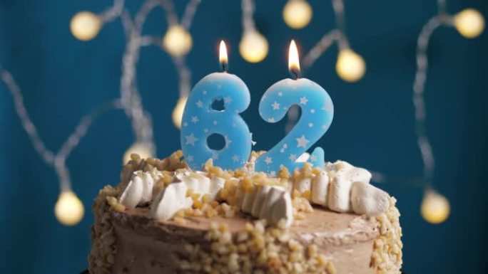 蓝色背景上有62号蜡烛的生日蛋糕。蜡烛着火了。慢动作和特写视图