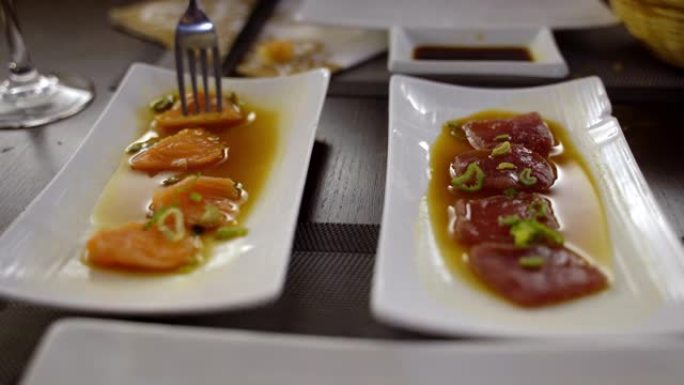两个白色盘子的特写镜头，上面放着新鲜的鲑鱼和金枪鱼切片，上面放着新鲜的葱和酱油。美味的日本餐厅，优质