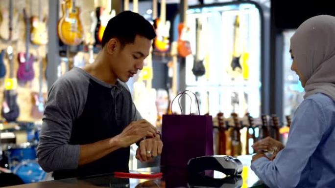 年轻的穆斯林男子使用智能手表在收银台通过非接触式交易付款