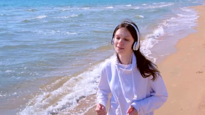 戴着耳机的女孩音乐在沙滩上慢跑运动进行户外训练。