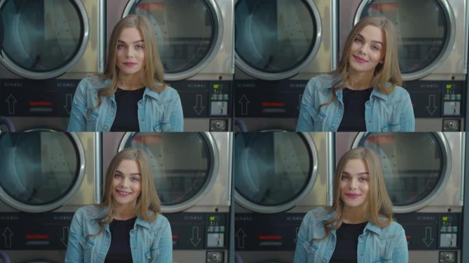 年轻微笑女子站在自助公共洗衣店的肖像。