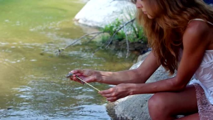 侧视图红发女孩在河岸用棍子印虾