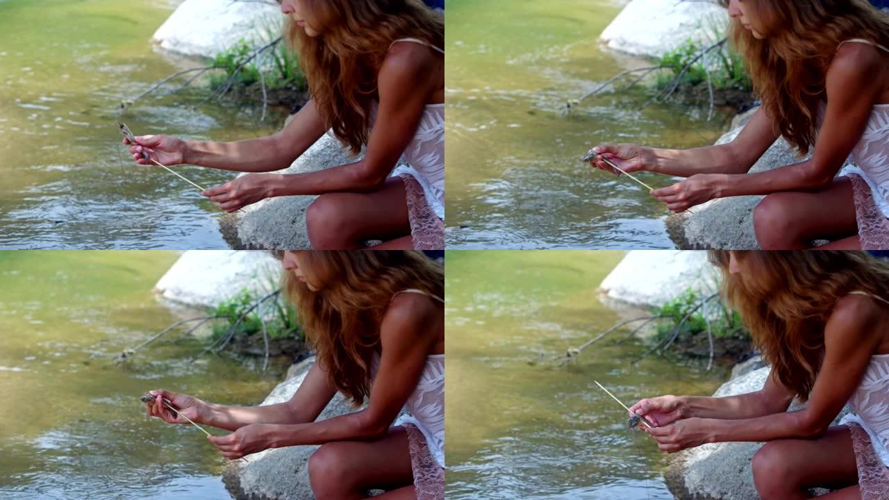 侧视图红发女孩在河岸用棍子印虾