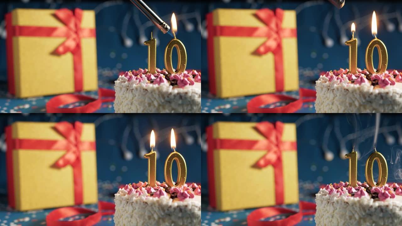 白色生日蛋糕10号点火器燃烧的金色蜡烛，带灯的蓝色背景和用红丝带绑起来的礼物黄色盒子。特写