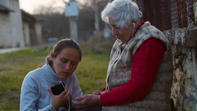 伸出援助之手。年轻女子用一套耳机和电话向祖母解释如何听音乐。