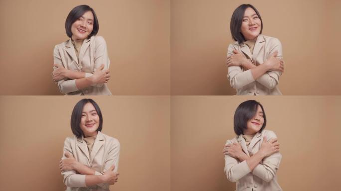 亚洲女商人微笑着拥抱自己的骄傲和幸福，孤立于米色背景。4k视频