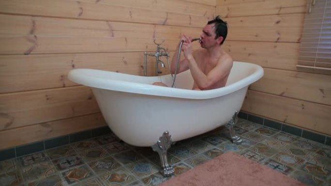 男人坐在浴室里，在淋浴喷头里唱歌