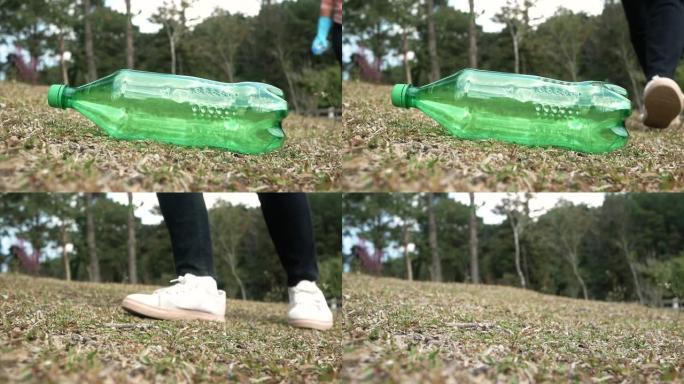 戴着手套的志愿者的近距离手从公园的草地上捡起一个塑料瓶。节约环境和制止塑料污染的概念。