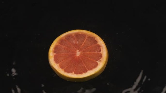 成熟多汁的柚子片落在覆盖着水的黑色表面上。慢动作。