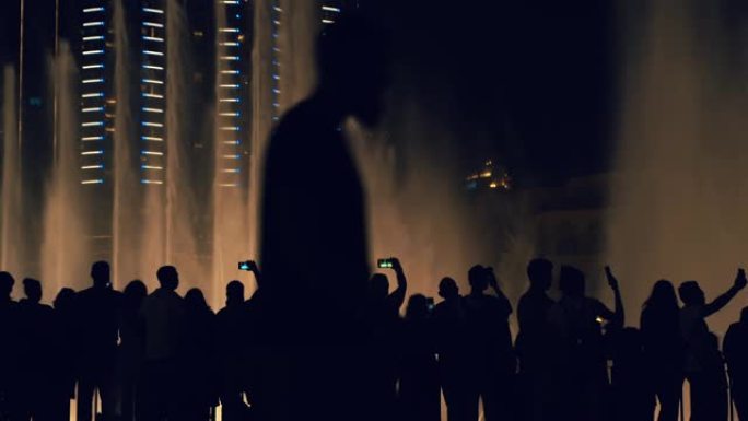 阿联酋迪拜夜间在智能手机上拍摄照片和视频的游客剪影