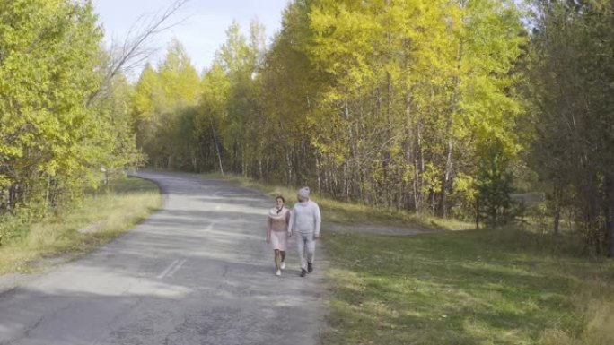 女人和一个男人沿着柏油路走过秋天的森林，俯视图