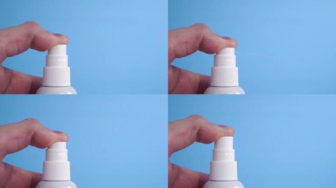 一个年轻人的手按下按钮，用白色塑料喷雾在蓝色背景上消毒