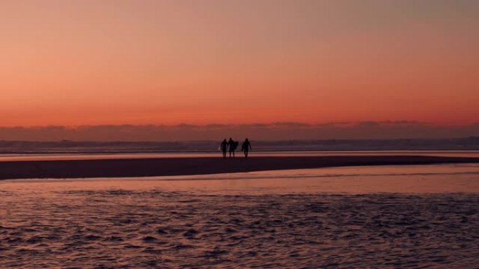 在金色的日落/日出上进行了一次惊人的冲浪之后，三个冲浪者从海上出来的惊人照片。