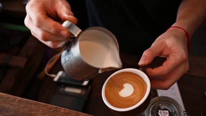咖啡师手的剪裁镜头试图将蒸牛奶倒入热咖啡中，以制作拿铁艺术。