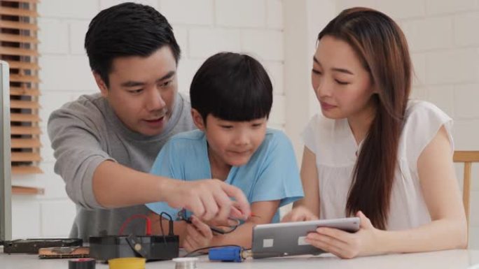 年轻的父母帮助他们的儿子在家组装电脑。妈妈在平板电脑上打开信息来帮助小男孩。科技、教育、家庭和创新理