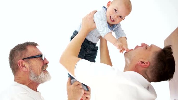 蹒跚学步的孩子从祖父身上摘下眼镜。父亲抱着婴儿大笑