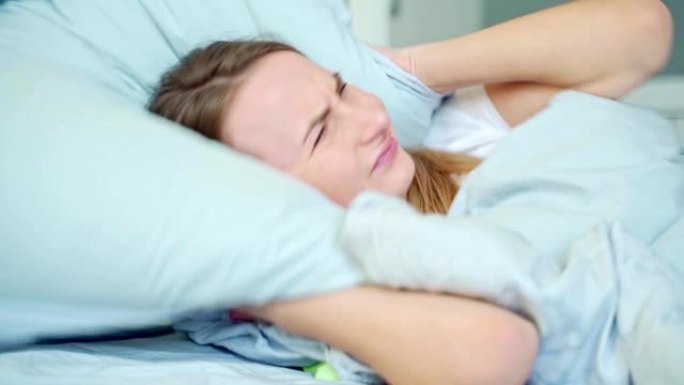 恼怒的女人试图睡觉被糟糕的嘈杂的房间邻居用枕头遮住耳朵，愤怒的女学生被吵闹的问题打扰醒来躺在床上失眠