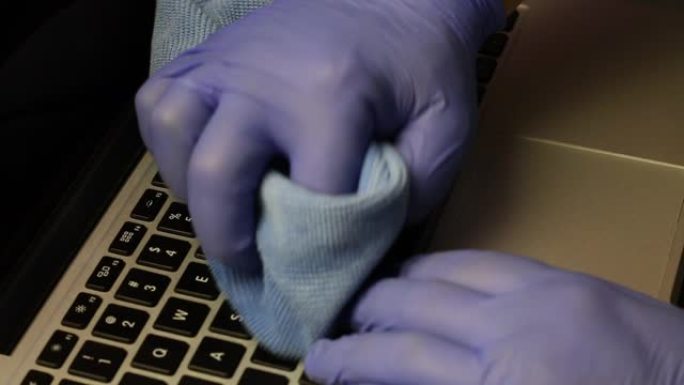 一个戴着橡胶手套的男人正在清洁他的笔记本电脑。他用特殊的餐巾擦拭笔记本电脑键盘。保护工作设备免受病毒