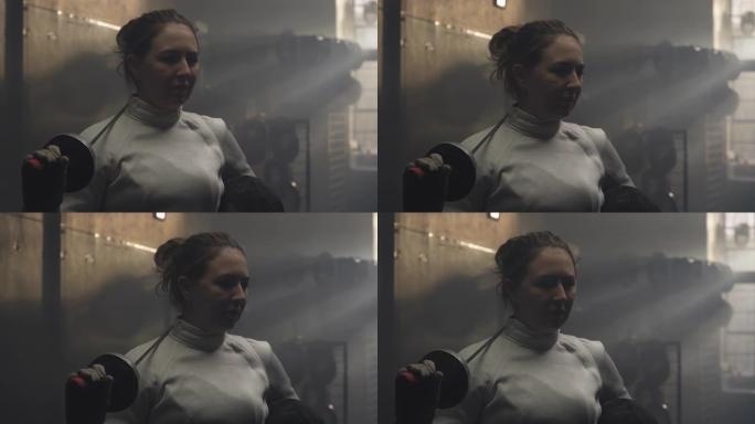 在黑暗多雾的更衣室里，一个穿着击剑装备摆姿势的女人