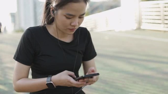 迷人的白人女运动员坐在城市日落的街道旁，在社交媒体交流上分享信息。戴耳机听音乐的女孩跑步者。