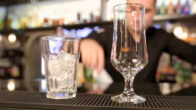 酒保将冰块放在夜总会酒吧柜台的水杯中