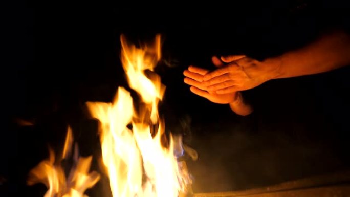 晚上，年轻游客的低视野在曼加尔 (mangal) 的篝火前擦手。男人在黑色背景下用金属火盆的火加热手