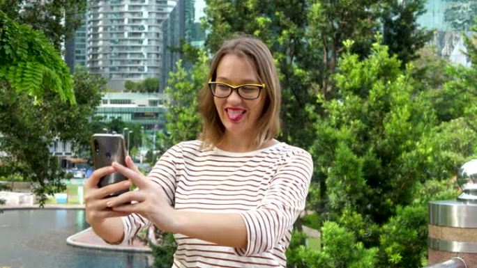 可爱的女性使用智能手机在城市公园自拍