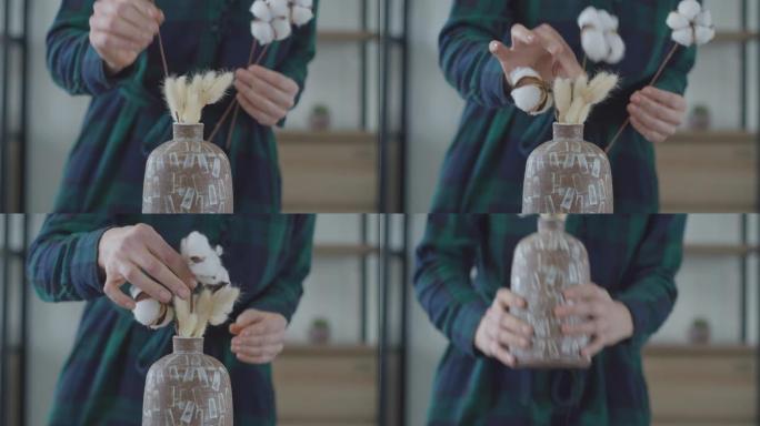 简约室内公寓中，女性双手在花瓶中组织棉花布。花瓶中的干燥植物。