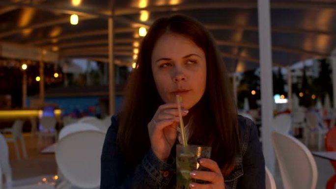 一名年轻女子晚上坐在街头咖啡馆里喝莫吉托。