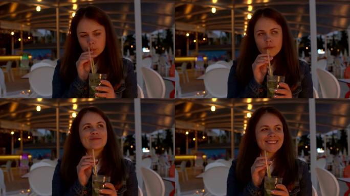一名年轻女子晚上坐在街头咖啡馆里喝莫吉托。