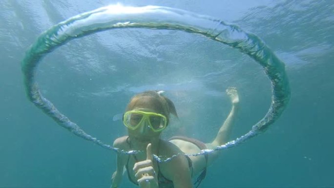 女人在水下玩泡泡。自由潜水者打破了在水下移动的环形气泡