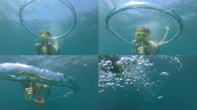 女人在水下玩泡泡。自由潜水者打破了在水下移动的环形气泡